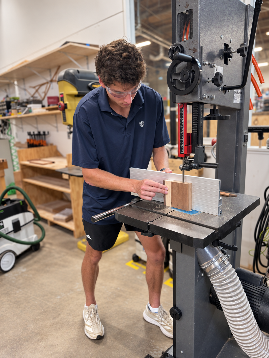 Trevor wearing safety glasses while working with wood at a bandsaw in a workshop.
